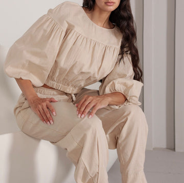 Model wearing beige Featherlight Duo Coords seated, showing off-shoulder top and relaxed-fit pants